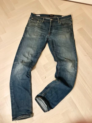 Blå jeans från Jack & Jones - Säljer ett par klassiska blå jeans från Jack & Jones i storlek W30. L32 . Jeansen har snyggt slitna detaljer, fem fickor och kontrastsömmar. Modellen är rak och passar perfekt till en avslappnad stil. Materialet är robust denim i bomull.