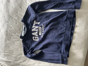 Blå sweatshirt från GANT med tryck - Snygg marinblå sweatshirt från GANT med stort vitt tryck på bröstet där det står 'GANT 1949 NEW HAVEN'. Tröjan har rund halsringning och långa ärmar. Perfekt för en avslappnad och sportig stil.