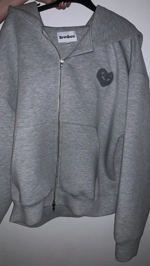 Grå zip-hoodie från StreetSpirit  - Säljer en grå hoodie från StreetSpirit i storlek L. Har inte använt den alls mer än att jag testat den och passade inte mig. Tröjan har dragkedja framtill, huva och två fickor. På bröstet finns ett broderat hjärta och på ryggen står StreetSpirit i mörkgrå färg. Perfekt för chill dagar och streetwear vibes. 