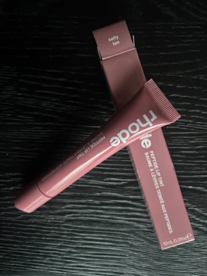 Rhode Peptide Lip Tint Salty Tan - Rhode Peptide Lip Tint i färgen Salty Tan, 10 ml. Kommer i en snygg tub med matchande förpackning i en rosa-brun nyans. Ger läpparna en naturlig tint och innehåller peptider för extra vård. Perfekt för dig som vill ha återfuktade och snygga läppar med lite färg.