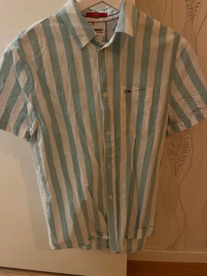 Randig skjorta från Tommy Hilfiger - Kortärmad linneskjorta med ränder. Bröstficka med diskret logga. Perfekt för dig som gillar en chill och stilren look. Passar er bra som är 175-185!