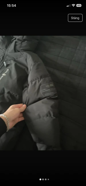 Svart pufferjacka från sail racing  - Säljer en svart pufferjacka från sail racing med huva och diskret logga på ärmen. Jackan har dragkedja framtill och är riktigt tjock och varm, perfekt för kalla dagar. Enkel och stilren design som funkar till det mesta.