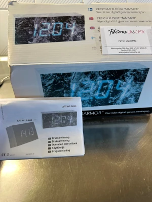 Designad Klocka 'Marmor' Digital Väckarklocka - Modern digital väckarklocka med marmormönster och LED-display. Visar tiden tydligt genom marmorliknande yta. Levereras i originalförpackning, dock med synliga skador på kartongen och mindre repor på baksidan. Komplett med bruksanvisning.