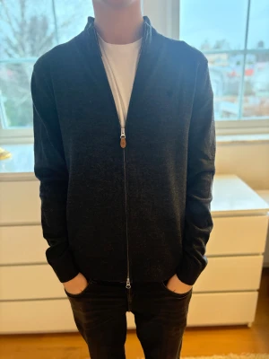 Mörkgrå kofta från Morris - Säljer min mörkgrå kofta från Morris i 100% merinoull. Modellen har hel dragkedja framtill, ribbad krage och muddar vid ärmslut. Perfekt att slänga på över en t-shirt för en chill och stilren look.