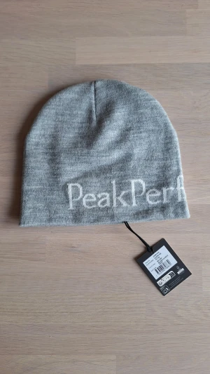 Grå Peak Performance mössa  - Snygg grå mössa från Peak Performance i tätstickad akryl och en mjukt stretchig känsla. Bekväm passform och kontrastfärgad jaqcuardstickad Peak Performance-logotyp.