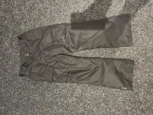 Svarta täckbyxor från 2117, stl 152 - Svarta täckbyxor från 2117 med clean skandinavisk design. Byxorna har flera fickor, justerbar midja och breda ben. Perfekta för vintern och håller dig varm och torr. Materialet är slitstarkt och vattenavvisande syntet. Hör av er om ni vill ha specifika bilder.