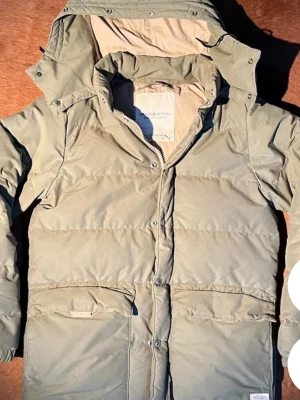 Ljusgrön dunjacka med huva - Snygg ljusgrön dunjacka från Denim & Supply Ralph Lauren med avtagbar huva, stora framfickor och dragkedja med tryckknappar. Jackan har en längre modell och quiltad design som håller värmen under kalla dagar.