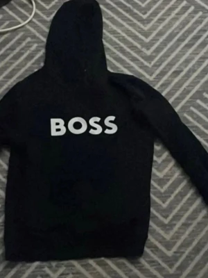Svart hoodie med BOSS-tryck - Svart hoodie från BOSS med stor vit logga på bröstet. Klassisk modell med huva och långa ärmar. Tillverkad i mjukt material som passar perfekt för en chill och avslappnad stil. Pris kan diskuteras, äkta hoodie, nytt skick