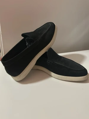 Mörkblå/svarta mockaloafers från Massimo Dutti - Säljer ett par stilrena svarta loafers från Massimo Dutti i mjuk mocka. Skorna har en klassisk design med vita gummisulor och diskreta sömdetaljer längs ovandelen. Sulan är en aning dammig men går lät att tvätta bort.