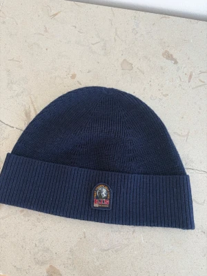 Mörkblå mössa från Parajumpers - Mörkblå ribbstickad mössa från Parajumpers med uppvikt kant och klassisk PJS-logga framtill. Tillverkad i mjukt material som håller värmen under kalla dagar. Perfekt accessoar för en stilren och sportig look.