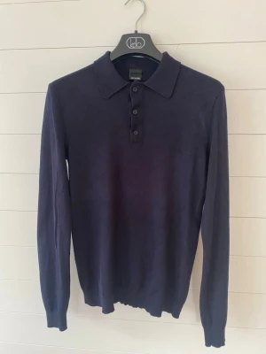 Mörkblå långärmad pikétröja - Snygg mörkblå långärmad pikétröja från only&son med klassisk krage och tre knappar framtill. Tröjan har en smal passform och är tillverkad i ett mjukt, tunt material som känns skönt mot huden. Perfekt för en stilren look.