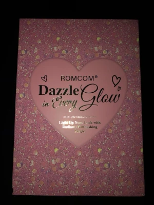 ROMCOM Dazzle in Every Glow highlighter - ROMCOM Dazzle in Every Glow är en highlighterpalett i en glittrig rosa förpackning med hjärtformad detalj. Paletten är designad för att ge ett strålande glow och innehåller flera nyanser för att framhäva ansiktets drag. Perfekt för dig som älskar shimmer och snygg förpackning.