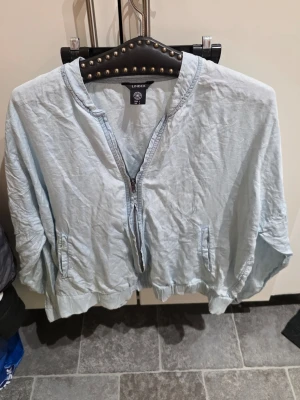 Ljusblå bomberjacka från Lindex - Ljusblå bomberjacka från Lindex med dragkedja framtill och två fickor. Jackan har en avslappnad passform och ribbade muddar vid ärmslut och nederkant. Tillverkad i ett lätt material, perfekt för lager på lager och streetwear.