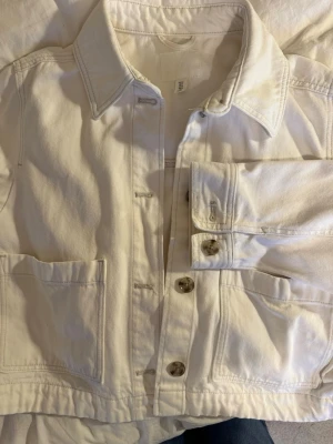 Vit jeansjacka från H&M - Snygg vit oversized jeansjacka från H&M. Raka ärmar, fickor och snygga knappar! Jackan är bara använd några fåtal gånger och visar inga tecken på användning! Kommer passa perfekt till våren/ sommaren!