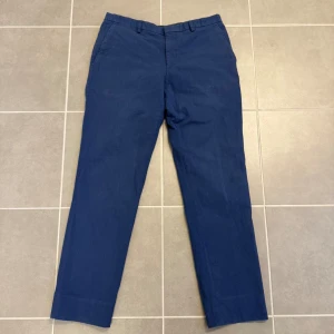 J.Lindberg Blå chinos med raka ben - Snygga blå chinos med klassisk passform och raka ben från J.Lindberg. Byxorna har bälteshällor och sidofickor, perfekta för en stilren look. Tillverkade i ett mjukt bomullstyg som känns bekvämt hela dagen.