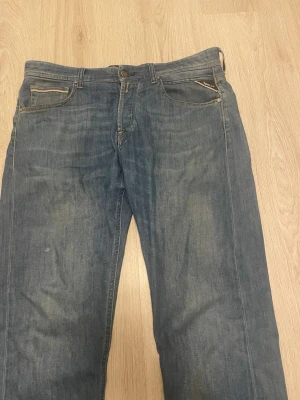 Blå jeans från Replay med raka ben - Snygga blå jeans från Replay med klassisk femficksdesign och raka ben. Jeansen har ljusa slitningar och detaljerade bakfickor med dekorativa sömmar. Tillverkade i denim med en autentisk tvättad look och läderpatch bak i midjan.