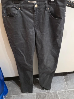Mörkgrå jeans med smal passform - Snygga mörkgrå jeans med smal passform och klassisk femficksdesign. Jeansen har normal midja, dragkedja och knapp framtill. Perfekta för dig som gillar en enkel och stilren look. Storlek 38 enligt lappen.