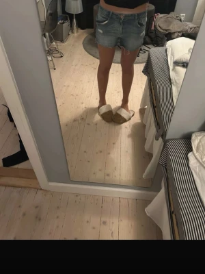 Blå jeansshorts med slitningar - Snygga blå jeansshorts med slitna detaljer och råa kanter. Klassisk femficksmodell med knapp och dragkedja framtill. Perfekta för varma sommardagar och en avslappnad stil.