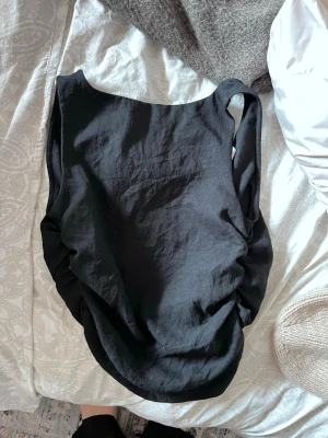 Svart ärmlös topp i linne - Säljer en svart, ärmlös topp med rund halsringning och lätt rynkade sidor. Toppen är tillverkad i linne & fin öppning i ryggen