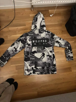 Svartvit hoodie WX//PRO med mönster - Snygg svartvit hoodie från WX//PRO med coolt collage-mönster och tryck på bröstet. Hoodien har huva och en stor magficka. Perfekt för dig som gillar streetwear och unika prints.