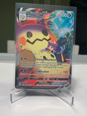 Pokémonkort Mimikyu VMAX Full Art - Säljer ett färgstarkt Mimikyu VMAX Pokémonkort med full art-design. Kortet har holografiska effekter och visar Mimikyu tillsammans med Acerola. Text på engelska och HP 300. Perfekt för samlare eller Pokémonfans.