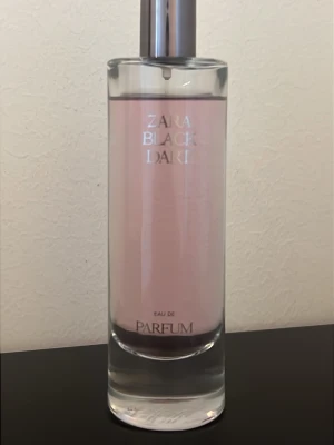 Zara Black Dart Eau de Parfum - Zara Black Dart Eau de Parfum med ljusrosa vätska i en stilren, cylindrisk glasflaska med silverfärgad spraykork. Flaskan har minimalistisk design och tydlig logotyp framtill. Perfekt för dig som gillar eleganta och moderna dofter.