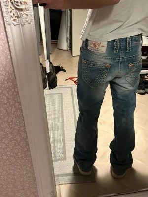 Blå True Religion jeans  - True Religion jeans  Blå jeans med tjocka kontrastsömmar och broderade bakfickor midjan är runt 70-80 w-29 och längden topp till tå är runt 80-90cm                                                                                                                   Knapparna är gröna på grund av ålder och naturlig oxidation i metallen, inte skada.         Hör av er vid frågor! 