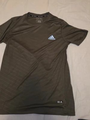 Svart Adidas t-shirt med diskreta ränder - Snygg svart t-shirt från Adidas med diskreta diagonala ränder och klassisk logga på bröstet. T-shirten har rund halsringning och är tillverkad i ett lätt och bekvämt material som passar perfekt till träning eller chill.