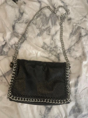 Svart axelväska med kedjedetaljer - Säljer min Tiamo-väska. Den är lite rostig, men handtaget som syns är fortfarande i fint skick, vilket gör den perfekt för den pyssliga eller vintage-älskaren som vill ge väskan nytt liv! ❣️  💰 Utgångspris: 90 kr – buda gärna! går med på de mesta!! Skickar inom 1-3 arbetsdagar (ibland helger) 📦
