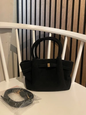 Handväska  - Svart handväska med gulddetaljer i mocka, längre band finns med.