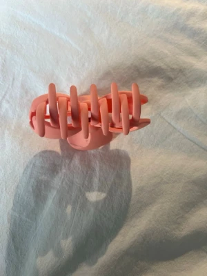 Rosa hårklämma med rosett - Söt hårklämma i matt rosa plast med en dekorativ rosett på sidan. Klämman har breda taggar som håller håret på plats och en mjuk, rundad form. Perfekt accessoar för att piffa upp frisyren med en gullig detalj, aldrig använd!