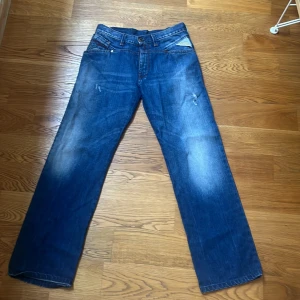 Replay jeans - Säljer ett par unika replay jeans i blå tvätt med snygga slitningar och raka ben. Jeansen har fem fickor, knappgylf och den ikoniska replay-lappen bak i midjan. Perfekt för dig som gillar tidlös streetstil och vill ha ett par jeans med autentisk känsla.