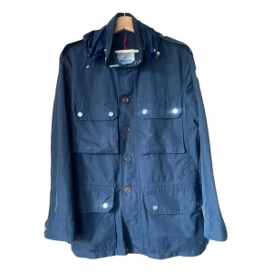 Marinblå vindjacka från Moncler - Snygg marinblå vindjacka från Moncler med fyra stora fickor framtill, knappar och tryckknappar. Jackan har en hög krage med snörning och Moncler-logga på ärmen. Materialet är lätt och syntetiskt, perfekt för blåsiga dagar. Luvan går att gömma bort också i en ficka som finns i kragen på jackan. Har äkta hets bevis och om man har fler frågor eller vill ha fler bilder är det bara att skriva,  pris går att diskuteras