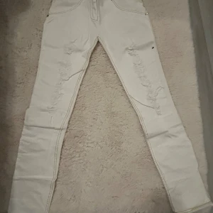 Vita skinny jeans från Freddy - Säljer ett par vita skinny jeans från Freddy med slitna detaljer framtill. Byxorna har klassiska fickor bak, guldfärgade sömmar och stretchigt material som sitter tajt. Perfekta för dig som gillar en clean men edgy look.