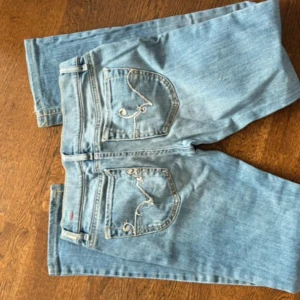 Diesel ljusblå jeans W27 L34 - Säljer ett par ljusblå Diesel jeans med snygga broderade detaljer på bakfickorna och klassisk Diesel Industry-märkning fram. Jeansen har raka ben och normal passform, tillverkade i mjukt denim med gul kontrastsöm och italienska flaggan broderad vid linningen.en fläck vid högra benet på framsidan från kål går säkert att tvätta bort.