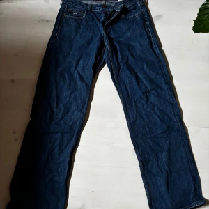 Tommy Jeans low waist raka blå jeans 27/32 - Klassiska blå jeans från Tommy Jeans med raka ben och normal passform. Jeansen har fem fickor, tydliga sömmar och en snygg mörkblå tvätt. Materialet är robust denim i bomull. Liten fransig detalj vid benslutet för en avslappnad look.