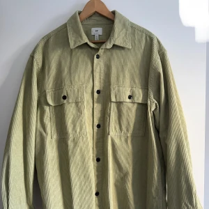Ljusgrön manchester overshirt  - Overshirt i ljusgrön manchester från H&M med klassisk krage, två stora bröstfickor med lock och svarta knappar framtill. Skjortan har lång ärm och en loose passform, perfekt att slänga över en t-shirt för en chill look.