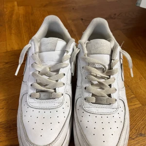 Nike Air Force 1 vita sneakers - Klassiska Nike Air Force 1 sneakers i helvitt skinn med perforerad tå, rund tå och platt sula. Skorna har snörning och den ikoniska swoosh-loggan på sidorna. Perfekta för dig som gillar en clean och tidlös streetstil.Original Nike Air Force 1 Low White  helt ny Jag fick den som present men har använt den bara några gånger för att den var liten. Den är i Storlek 39