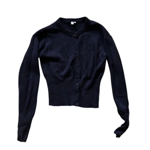 Svart kofta - Nelly - Snygg svart kofta med ribbad midja och knappar hela vägen framtill och rund halsringning. Perfekt att styla med jeans eller kjol för en cool look.