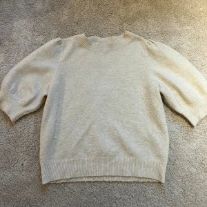 Beige stickad tröja Vero Moda XS - Snygg beige stickad tröja från Vero Moda i storlek XS. Tröjan har puffiga trekvartsärmar och ribbade muddar vid hals, ärmslut och nederkant. Perfekt för dig som gillar en enkel men trendig look med lite volym på ärmarna.