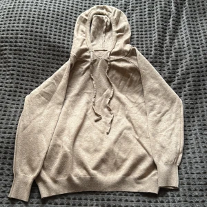 Beige hoodie med snörning, strl 36 - Snygg beige hoodie med huva och snörning framtill. Tröjan är stickad och har ribbade muddar vid ärmslut och nederkant. Perfekt för dig som gillar en chill och enkel stil. Passar dig som vill ha en neutral färg och mjukt material. Den är väldigt liten i storleken så skulle säga att de är xs.