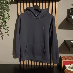 Mörkblå hoodie från Polo Ralph Lauren - Säljer en stilren mörkblå hoodie från Polo Ralph Lauren med klassisk röd logga broderad på bröstet. Passar dig som är mellan 165-175, en perfekt hoddie nu när dom kallare tiderna kommer!!! Kan själv klart går ner i pris vid en snabb och smidig affär!