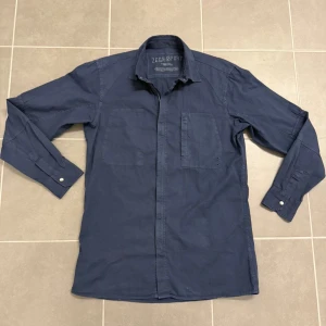 Mörkblå jacka från Zegna - Snygg mörkblå jacka från Zegna i storlek S. Skjortan har två bröstfickor, klassisk krage och långa ärmar med knappar vid manschetterna. Materialet är mjukt och känns som bomull, och den har en diskret dragkedja framtill för extra edge.