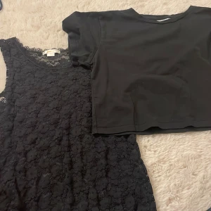 Svart spetsklänning från Gina Tricot - Supersnygg svart ärmlös spetströja från Gina Tricot. Tröjan har ett genomgående spetsmönster och rund halsringning. Tillsammans med den kommer det en kortare, magtröja i svart färg. Tröjorna kommer i ett pack då tanken är att man har den spetsiga tröjan under den korta t shirten, men båda är snygga hur som.