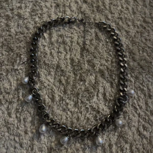 Chunky silverhalsband med pärlor - Stilrent halsband med grov silverfärgad kedja och sju droppformade vita pärlor som hänger längs länkarna. Perfekt statement piece för att lyfta vilken outfit som helst.