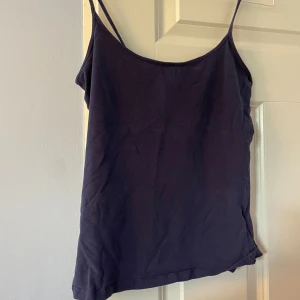 Mörkblå linnetopp från H&M - Säljer en enkel och stilren mörkblå linnetopp från H&M Basic. Toppen har smala axelband och ärmlös design, perfekt för varma dagar. Materialet är mjuk bomull som känns skönt mot huden. Passformen är normal och toppen är lätt att matcha med allt.