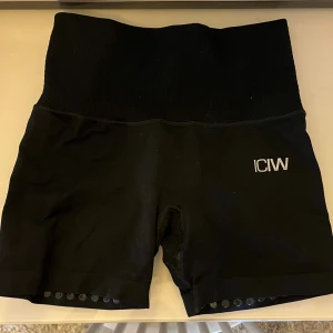 Svarta träningsshorts från ICANIWILL - Svarta högmidjade träningsshorts från ICANIWILL med ribbad midja och logga framtill. Shortsen har silikonprickar på insidan av bensluten för extra grepp och en liten dragkedja vid nedre rygg. Snygg och tight passform, perfekta för gymmet eller löpning.