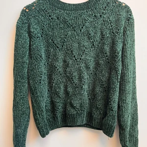 Grön stickad tröja med hålmönster - Mysig grön stickad tröja med snyggt hålmönster och ribbade muddar. Tröjan har rund halsringning och långa ärmar, perfekt för lager på lager under kyliga dagar