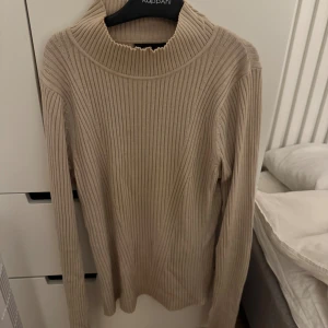 Beige ribbad polotröja från KappAhl - Säljer en beige ribbad polotröja från KappAhl i storlek S. Tröjan har lång ärm, hög krage och är tillverkad i ett mjukt stickat material. Perfekt för lager-på-lager och passar snyggt till både jeans och kjol.