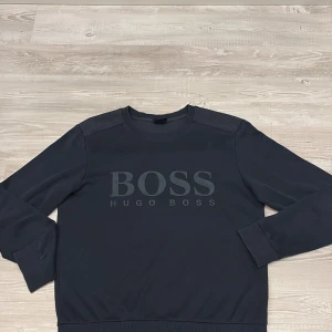 Mörkblå sweatshirt från Hugo Boss - Snygg mörkblå sweatshirt från Hugo Boss med stort logotryck framtill. Tröjan har rund hals, ribbade muddar och axelpartier i kontrastmaterial. Slim fit-modell som sitter tajt och stilrent. Perfekt för dig som gillar klassisk streetstyle.